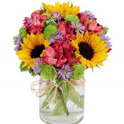 Reminiscent of strolling through a field of flowers, this colorful arrangement captures features magnificent sunflowers, alstroemeria and poms set in a trendy mason jar with a natural raffia bow.